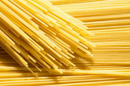 background of long raw yellow spaghetti pasta in horizontal plane, and bandle of macaroni on topの写真素材