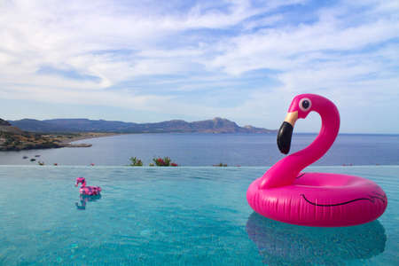 large and small pink inflatable pink Flamingo with a black beak floats in the pool at an altitude overlooking the sea and mountains. Pool party. Cocktail party.の写真素材