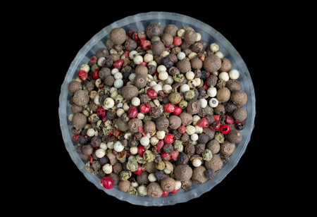 Glass plate of a mixture of dry pepper peas black, red, white colors isolated on black background....