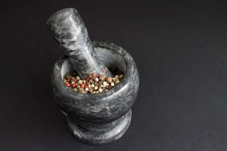 gray marble mortar and spice hammer with a mixture of dry peppers of different colors on a black backgroundの写真素材
