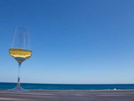Glass of white wine on the table with reflection of the beach inside, sky and sea on the background.の写真素材