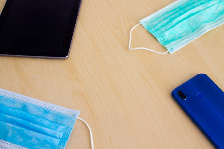 Blue and green mask smartphone and digital tablet lying in corners on wooden tableの写真素材