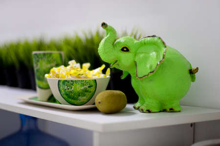 OMSK, RUSSIA, MAY 08, 2020: Green elephant figurine. It stands on a shelf next to a kiwi and a mug of tea and sweets.のeditorial素材