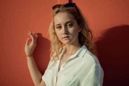 A girl in a white shirt poses against an orange wall. Blonde in sunglasses. The girl's portrait is bright.の写真素材