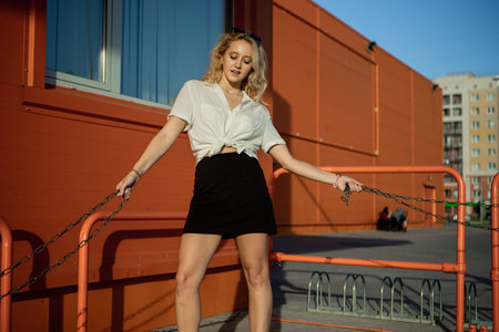 A girl in a white shirt poses against the background of an orange building. The blonde in sunglasses...