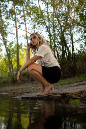 Girl near the water. A blonde woman in a white shirt poses on the Bank of a river or lake.の写真素材