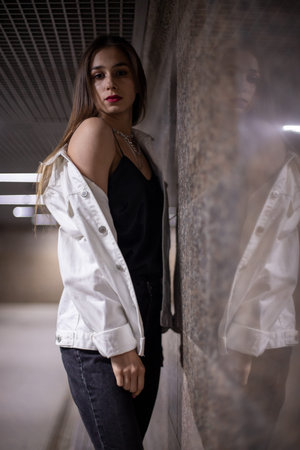 A teenage girl is facing the wall. Brunette in the underpass at night, reflection from the wall. A...