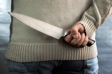 An evil man holds a knife behind his back, waiting for the victim. A maniac and a rapist with a gun.の写真素材