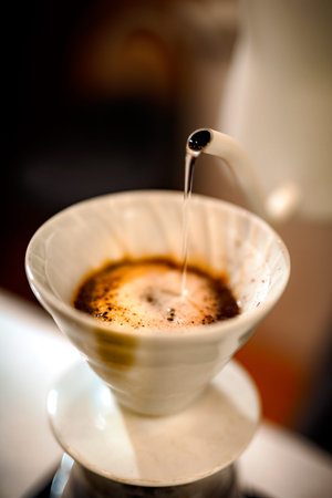 barista pouring hot water on rough brown bubbles coffee through drip filter, home brewing processの写真素材