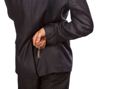 Man in dark grey busines suit standing isolated on white background with keys in hand behind his back.の写真素材