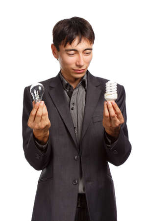 Young businessman in dark grey coat and steel-blue shirt standing with two light bulbs in his hands isolated on white backgroundの写真素材
