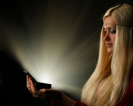 Beautiful young blonde longhaired woman with glowing box on black backgroundの写真素材