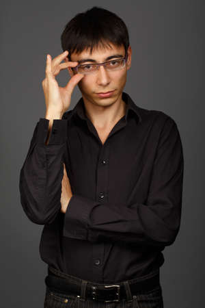 Beautiful young man standing in black shirt with glasses that he correcting with his handの写真素材