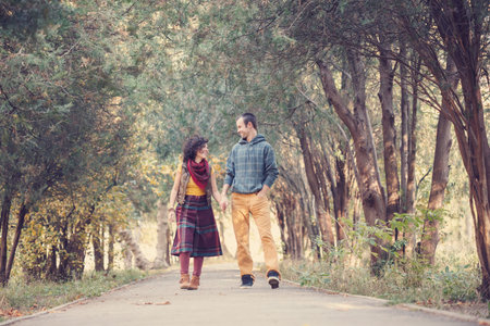 Loving couple in bright clothes walking along park alley holding hands and looking at each other