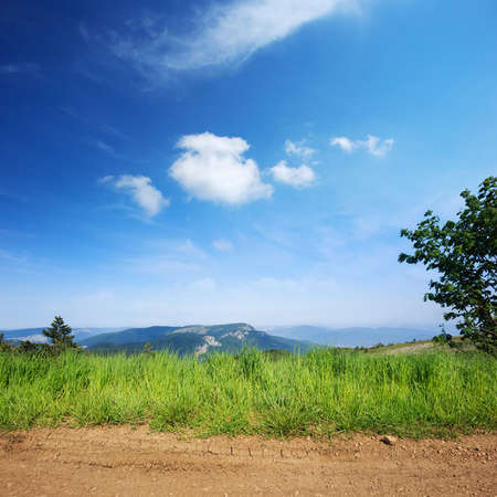 View of Crimean mountains with rural road and grass on foregroundの写真素材