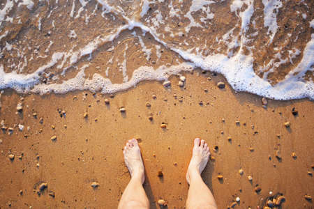Man's legs on the sand beach and sea waves at sunsetの写真素材