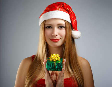 Beautiful young woman in santa claus suit with little gift box on gray backgroundの写真素材