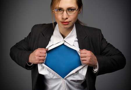 Beautiful young woman in business suit and glasses with hero concept on grey backgroundの写真素材