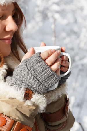 Beautiful young smiling woman in gray fingerless knitted mittens, cap and coat with white fur...