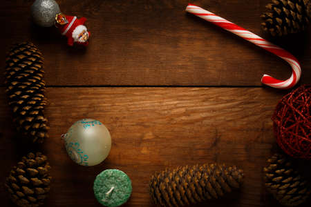Beautiful christmas frame decoration from peppermint candy cane stick, christmas balls, candle, santa claus decor, fir cones and pinecones at brown wooden background.の写真素材