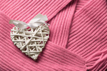 Beautiful white handmade wattled from rattan wooden valentine's day heart decoration with bow lays on pink woollen scarf background. Copyspace.の写真素材