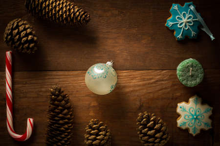 Beautiful christmas frame decoration from peppermint candy cane stick, christmas ball, candle, showflake shaped and patterned bisquit cookies, fir cones and pinecones at brown wooden background.の写真素材