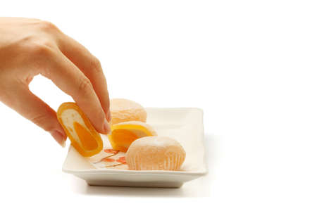 Beautiful elegant female hand taking mango mochi dessert from white square ceramic plate with japanese rice cakes isolated on white background.の写真素材