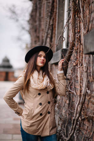 Street fashion concept. Vintage portrait of young woman in spring coat and hat. Flattering hair.の写真素材