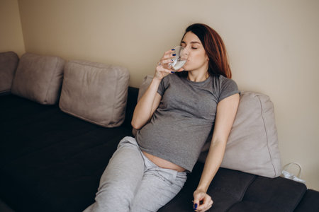 Close-up Of Pregnant Woman Hand With Glass Of Water And Vitamin Pillの写真素材