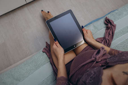 Happy pregnant woman using digital tablet with blank screen sitting on sofa. Young expectant lady surfing net, reading about baby care, buying goods for newborn. Online shopping, pregnancy conceptの写真素材