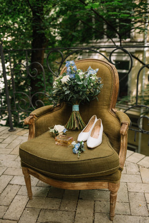Brides wedding shoes with a bouquet with roses and other flowers on tha arm chairの写真素材