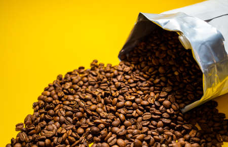 coffee beans poured from the pack on a yellow backgroundの写真素材