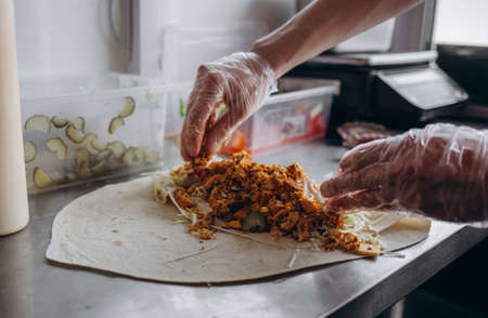 Men's hands wrapping traditional shawarma wrap with chicken and vegetablesの写真素材