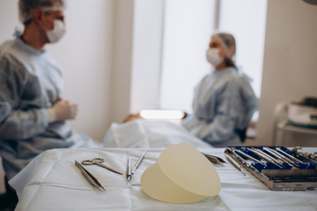 Nurse hand taking surgical instrument for group of surgeons at background operating patient . breast augmentation.の写真素材