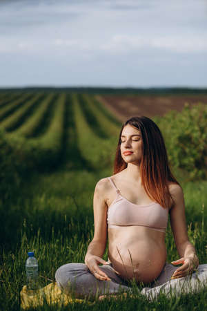 Closeup of charming pregnant woman doing yoga workout in parkの写真素材