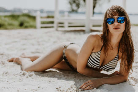 Beautiful sexy young woman with perfect slim figure with long dark hair and wet bathing suit fashion in stylish glasses from the sun is sunningの写真素材