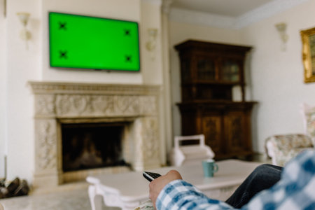Blank green screen TV with defocused female hand holding remote control.