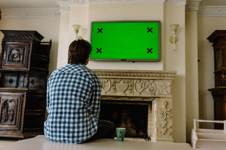 Back view of young couple sitting on chairs looking at tv with green screen, eating popcorn with the cat watching them.の写真素材