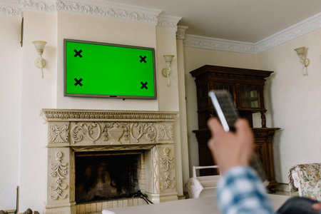 Blank green screen TV with defocused female hand holding remote control.