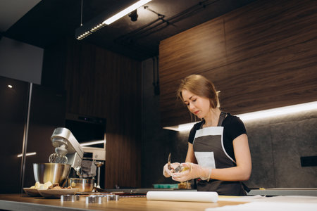 Pastry chef confectioner young caucasian woman with kitchen bowl on kitchen table. Cakes dessert makingの写真素材