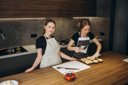 Front view of two confectioners cooking desserts. Beautiful women wearing white and black uniform....
