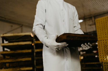 Proud of his baked goods. Handsome young man in apron holding basket with baked goods and smiling while standing in bakery shopの写真素材
