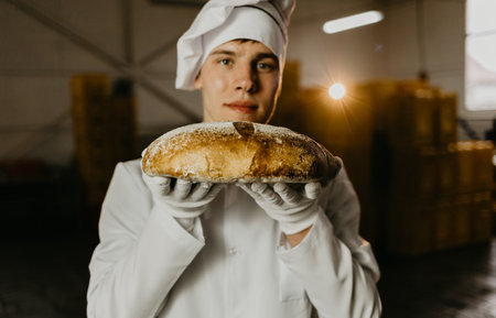 Young happy female worker in sterile cloths holding freshly baked cookies on tinplate inside food production factory.の写真素材
