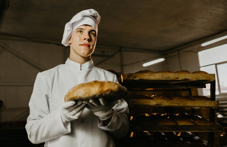 man with fresh bread in his hands, baker in apron and shirt giving hot bread on black backgroundの写真素材