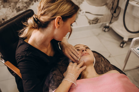 Close up of hands of cosmetologist making botox injection in female lips. She is holding a syringe. The young beautiful woman is receiving procedure with enjoymentの写真素材