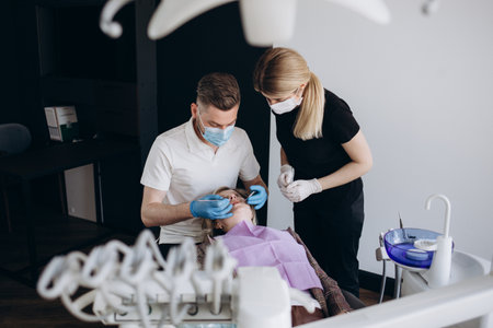 Modern dentistry private clinic with professional equipment. Dentists working with client's teeth. woman lying on dentist cahir. Doctors wearing in medical caps, unforms and masks.の写真素材