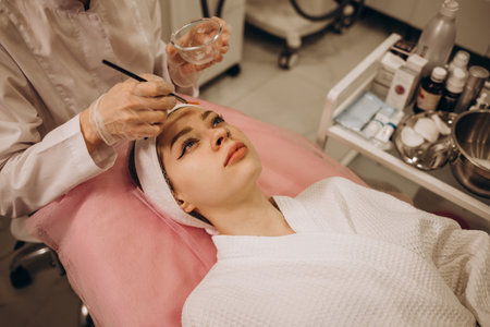 The cosmetologist applies a facial gold mask to the woman's face. Cosmetology and facial skin care in beauty salon. gold mask. cosmetic procedureの写真素材