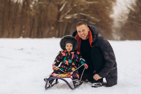 Father and daughter sitting on sled in snow field, smiling, portrait.の写真素材