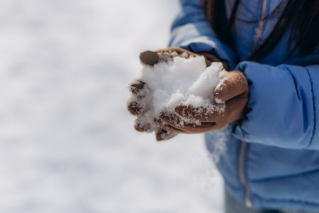 A young woman wearing mittens holds snow in her hands. close upの写真素材