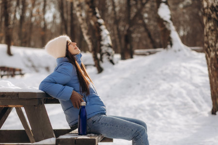 Happy young woman with cup of hot beverage sitting on bench and looking at copy space.の写真素材